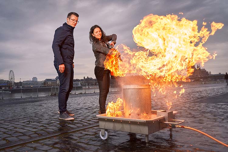 Eine Teilnehmerin führt unter Aufsicht des Trainers eine intensive Feuerlöschübung am Übungsbehälter durch.