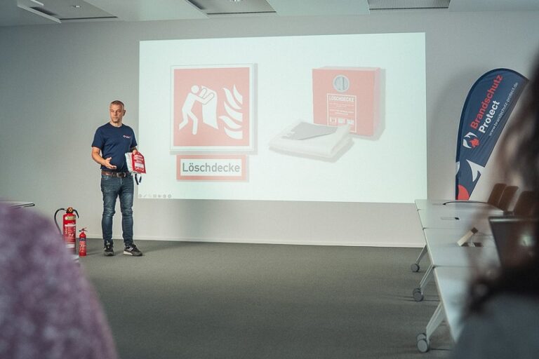 Ein Trainer präsentiert in der theoretischen Schulung der Brandschutzhelfer Ausbildung Köln den korrekten Einsatz der Löschdecke.