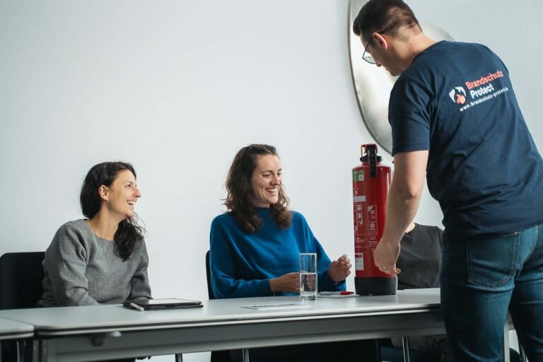 Der Dozent erklärt zwei Teilnehmerinnen die Funktionsweise eines Wasserfeuerlöschers.